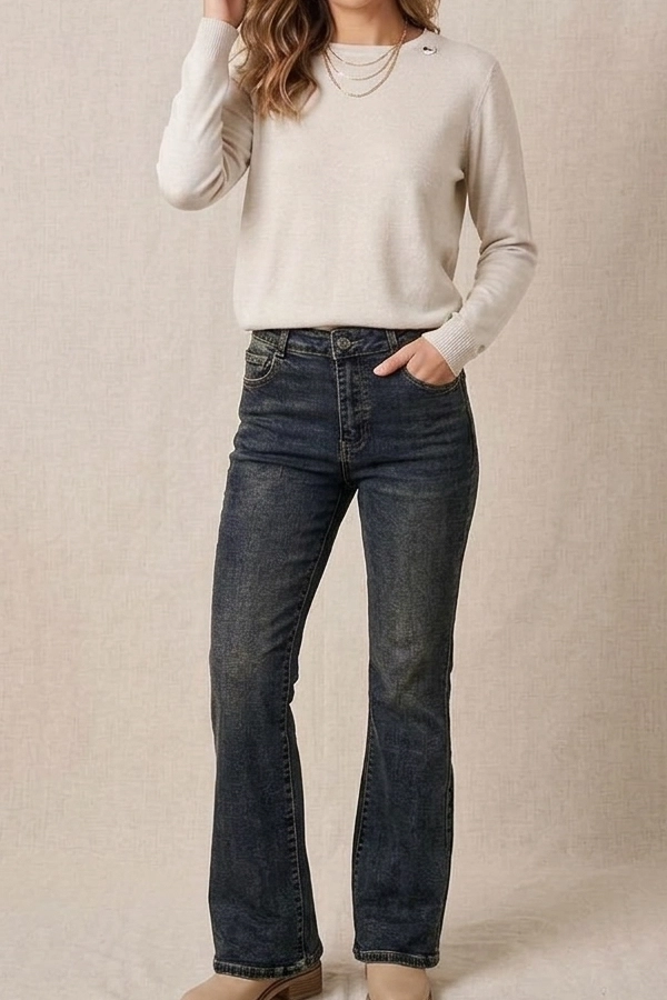 Woman styling dark wash high waist flare jeans with a cream knit sweater.